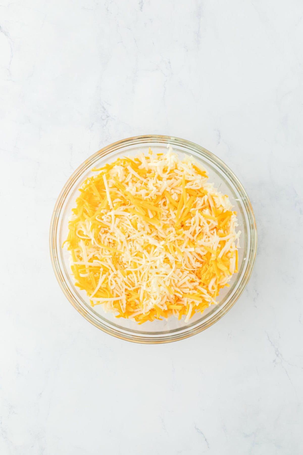 Shredded cheeses in a glass bowl on white countertop