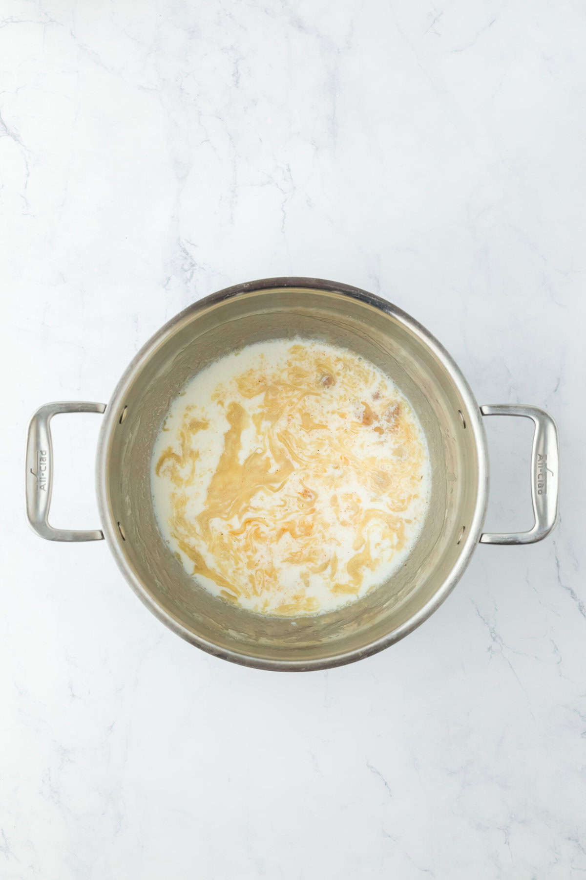 Milk and seasoning added to a roux in a pot on white countertop.