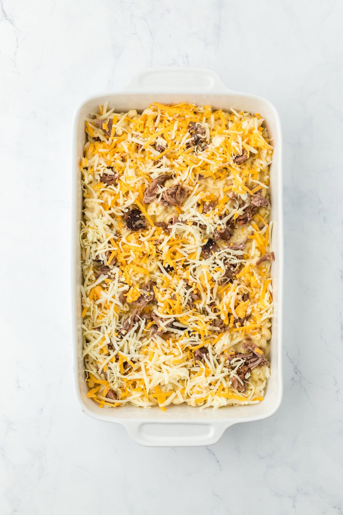 Half of macaroni in a casserole dish with brisket sprinkled on top