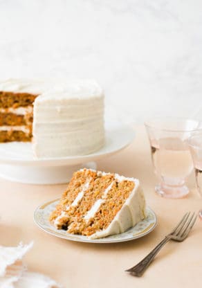 A slice of carrot cake sitting on vintage plate ready to serve with large cake in background