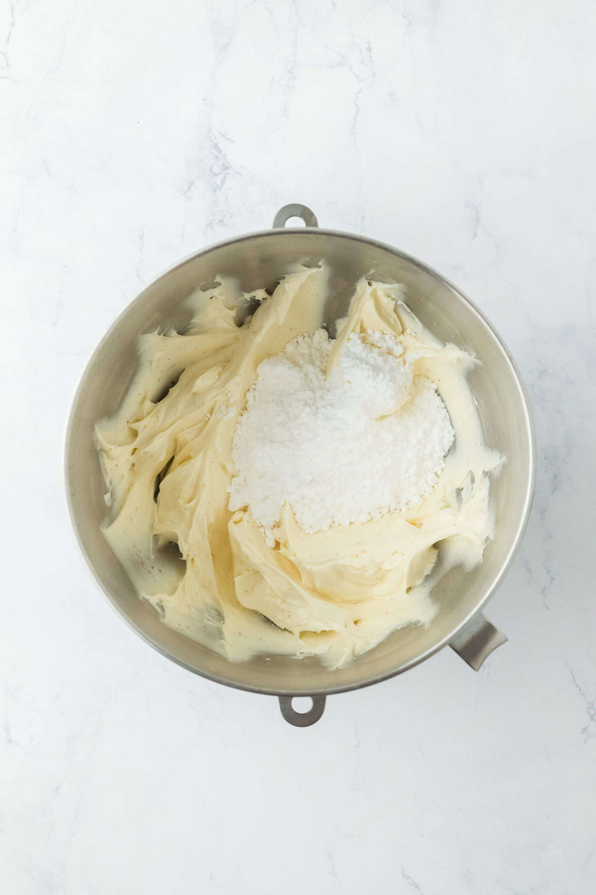 Powdered sugar added to cream cheese and powdered sugar in bowl