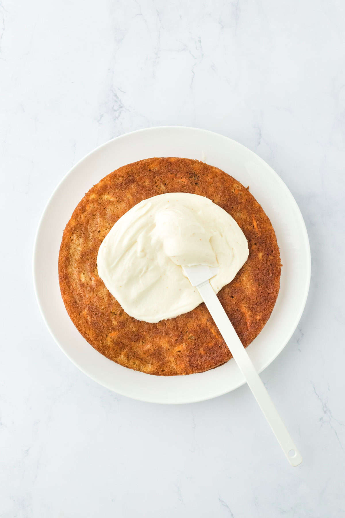 Frosting being spread on layer of carrot cake