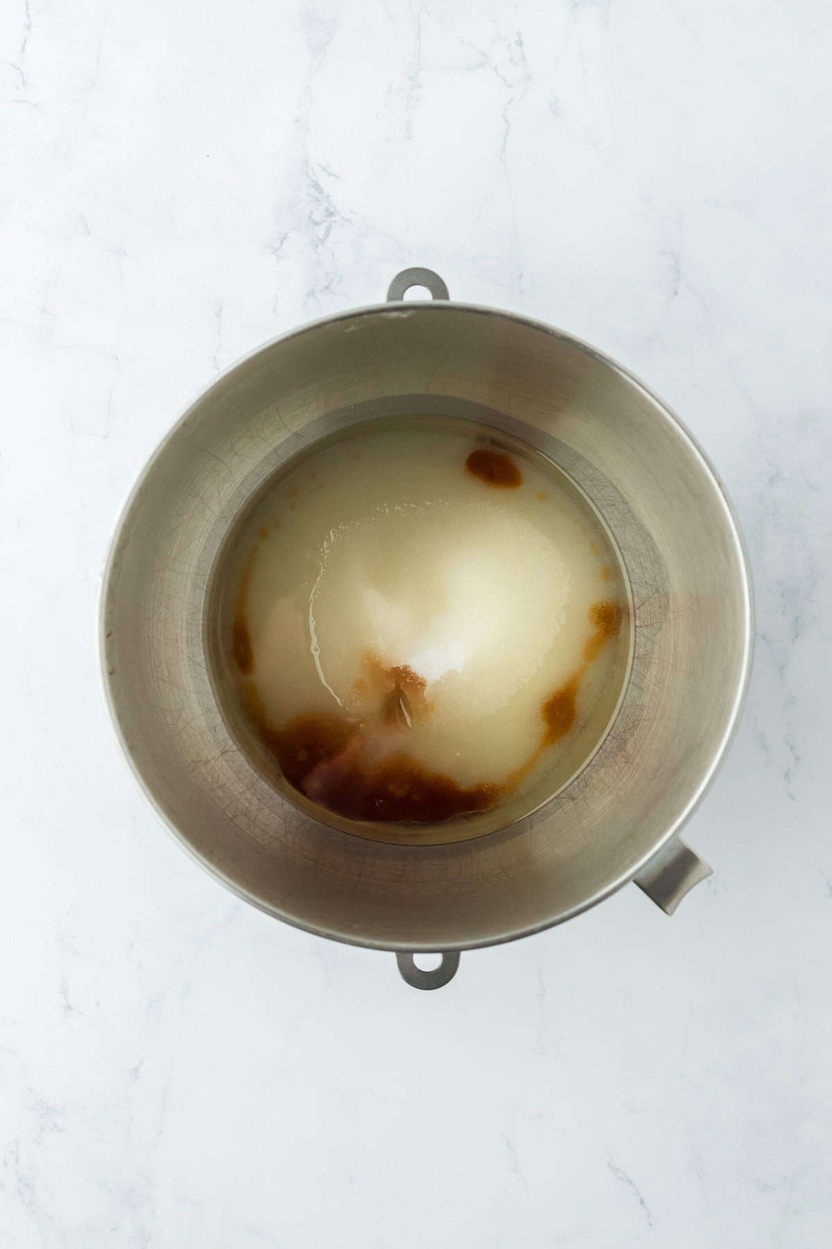 Sugar, oil, eggs and vanilla in a stand mixer bowl on white countertop