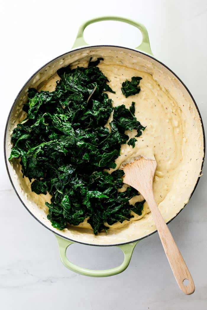 Thawed spinach being added to decadent cream sauce to show how to make creamed spinach recipe