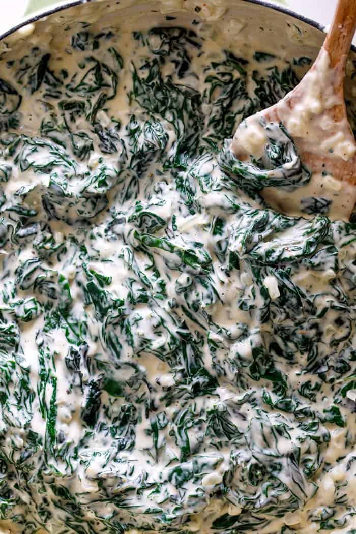 A close up of spinach being tossed in thick cream sauce