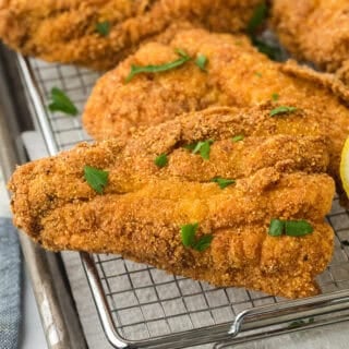 A close up of the best fried catfish fillets on a wire rack draining after frying with lemon wedge in the background