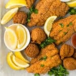 Deep fried catfish with hush puppies on a white surface with lemon wedges and parsley sprinkled on top