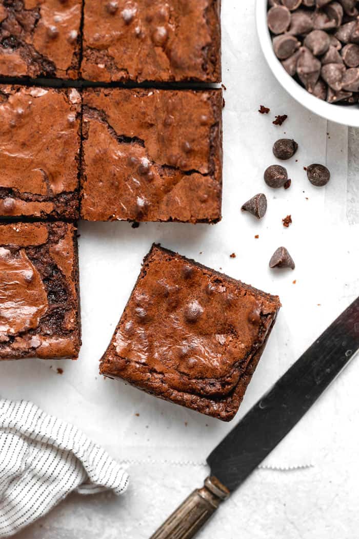 A close up of a cut batch of brownies with one cut from the batch with chocolate chips nearby