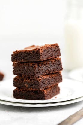 A stack of four fudgy brownies on a white plate ready to enjoy