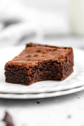 A chewy brownie on a white plate with a bite taken out