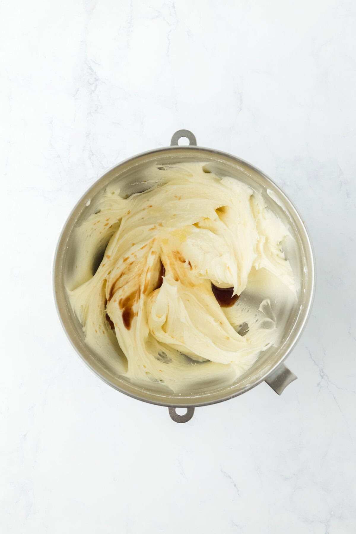 Pineapple and vanilla being added to stand mixer to mix frosting on white countertop