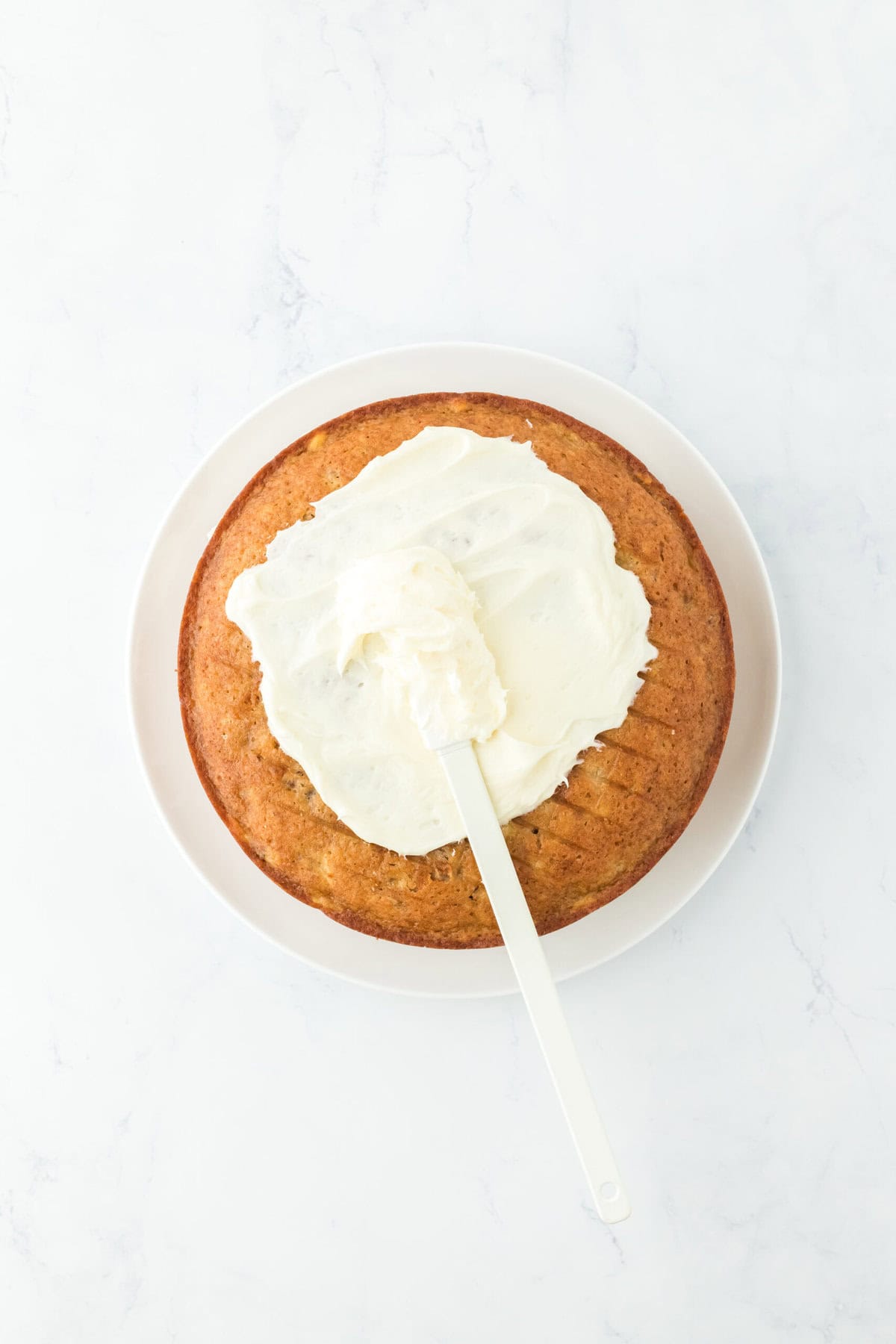 Spreading of frosting on layers of cake on white countertop