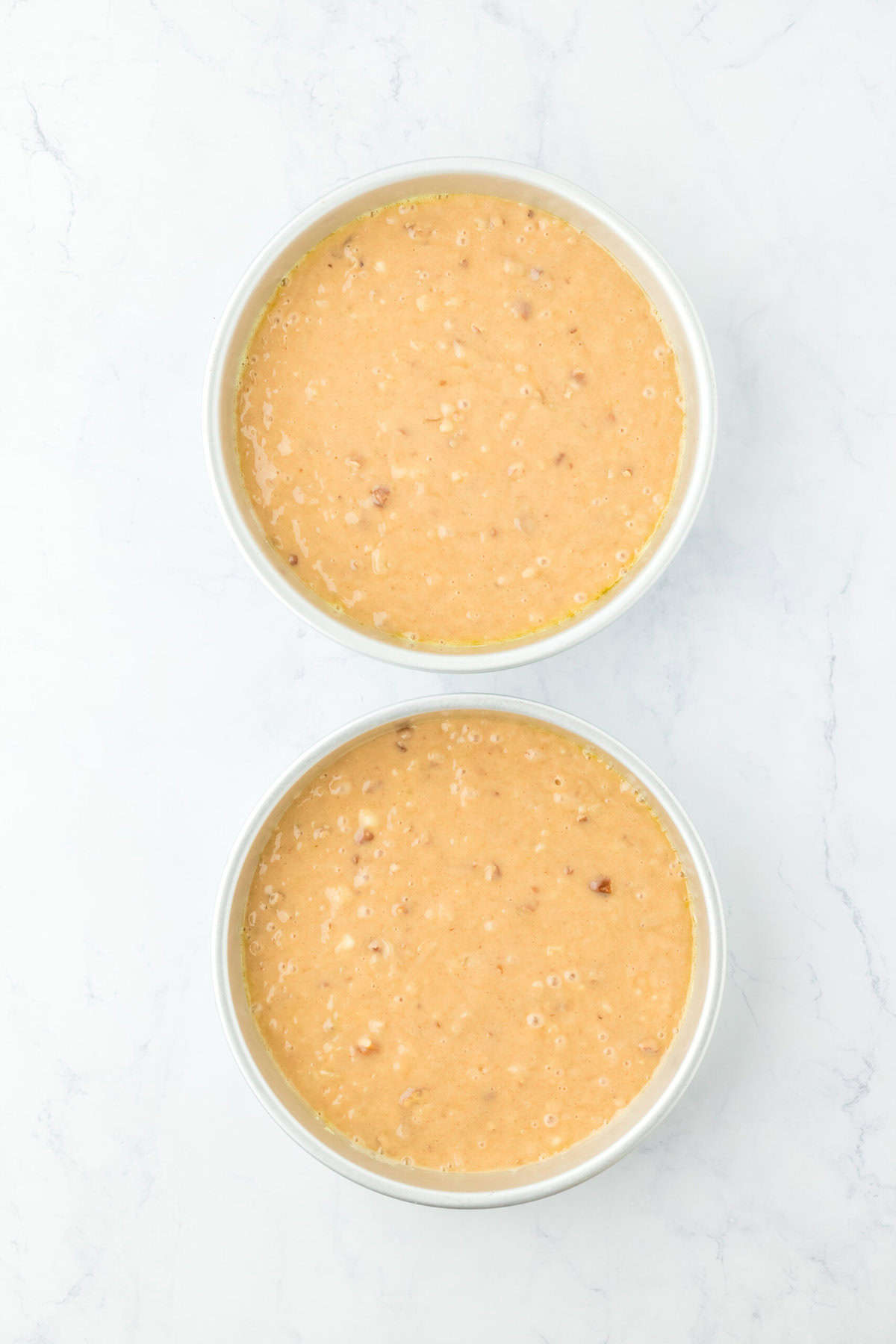 Hummingbird cake batter divided into two cake pans before baking on white countertop