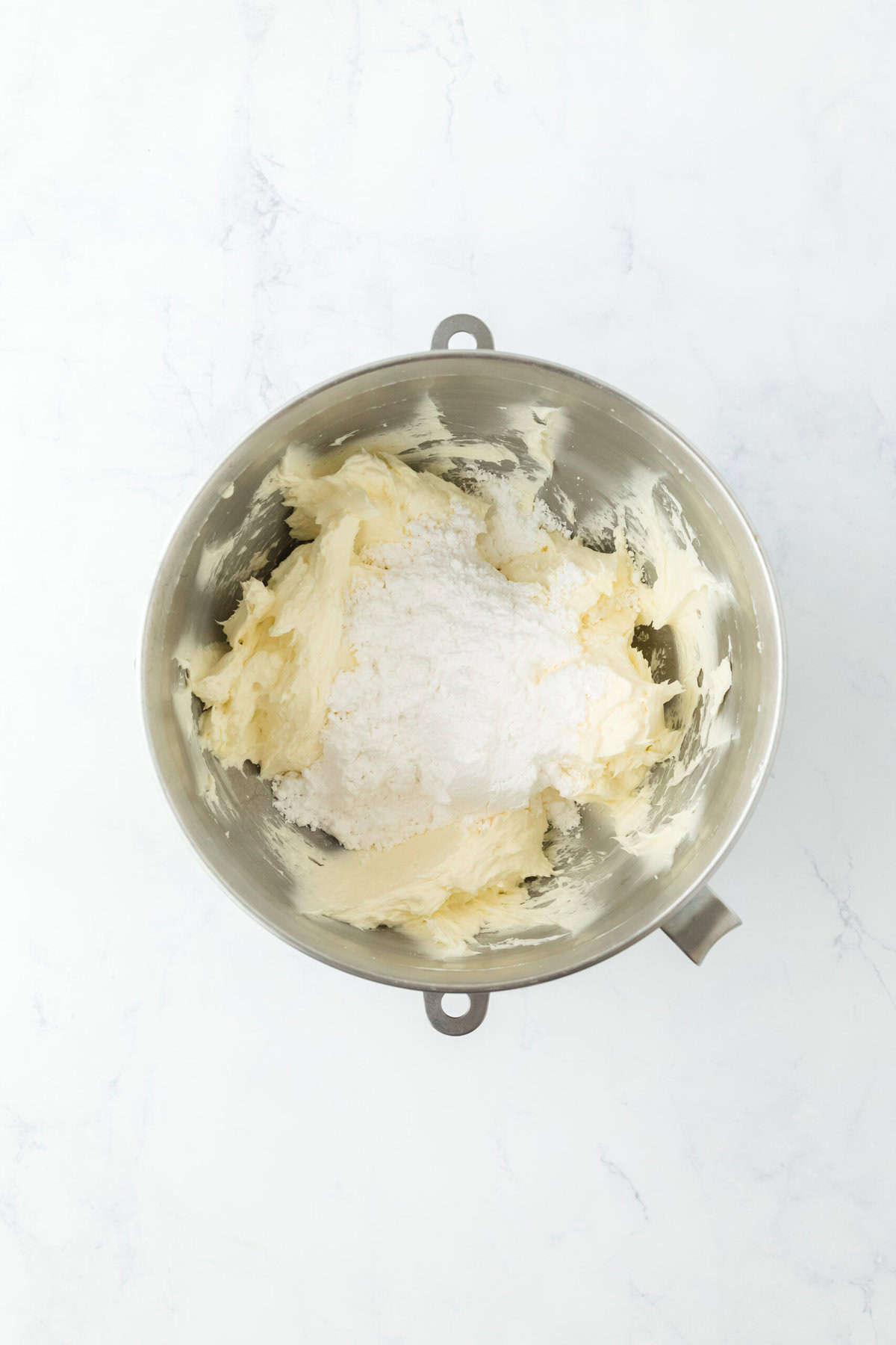 Confectioner's sugar added to butter and cream cheese in stand mixer