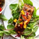 A close up of jerk seasoned salmon fillet with fruit salsa over spinach