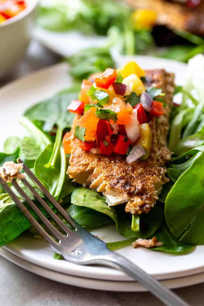 Delicious jerk salmon fillet topped with fruit salsa over healthy greens being eaten for dinner