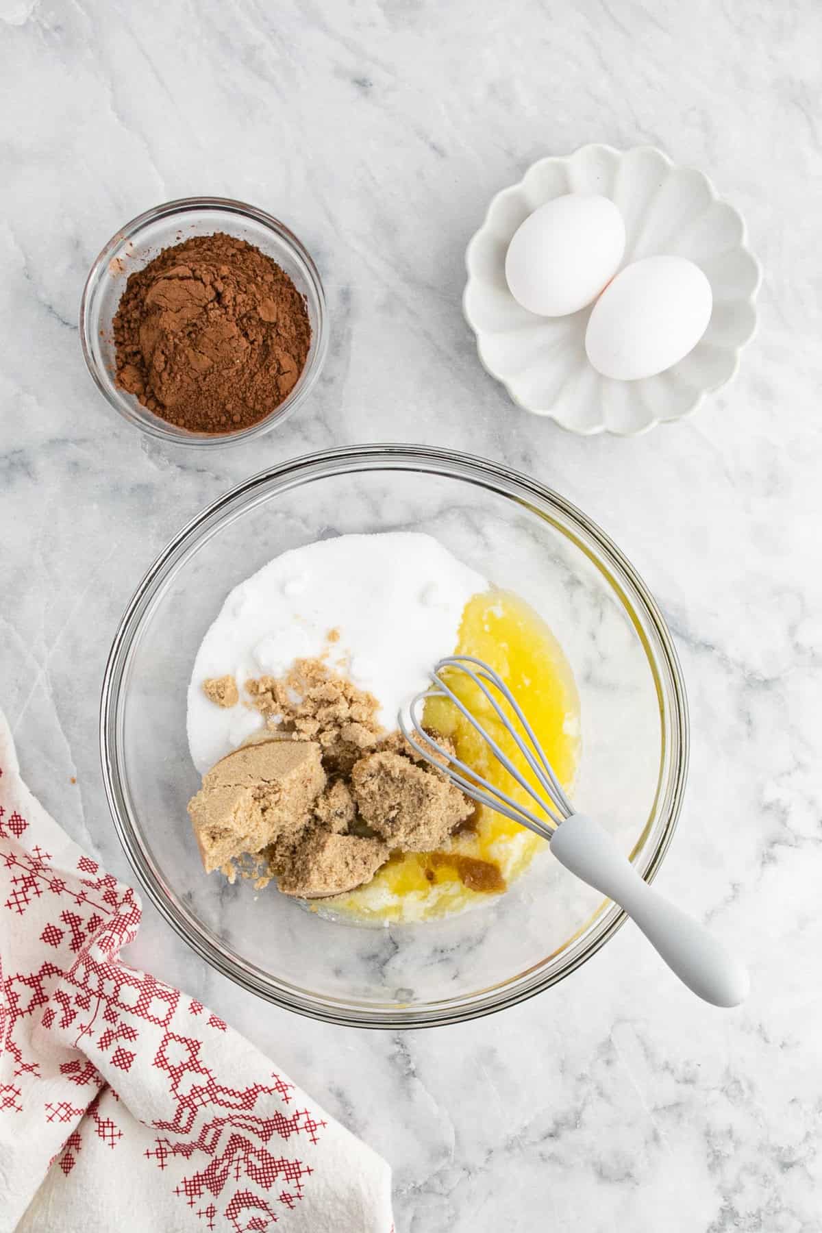 Brown sugar and granulated sugar along with melted butter in glass bowl with a whisk on marble countertop