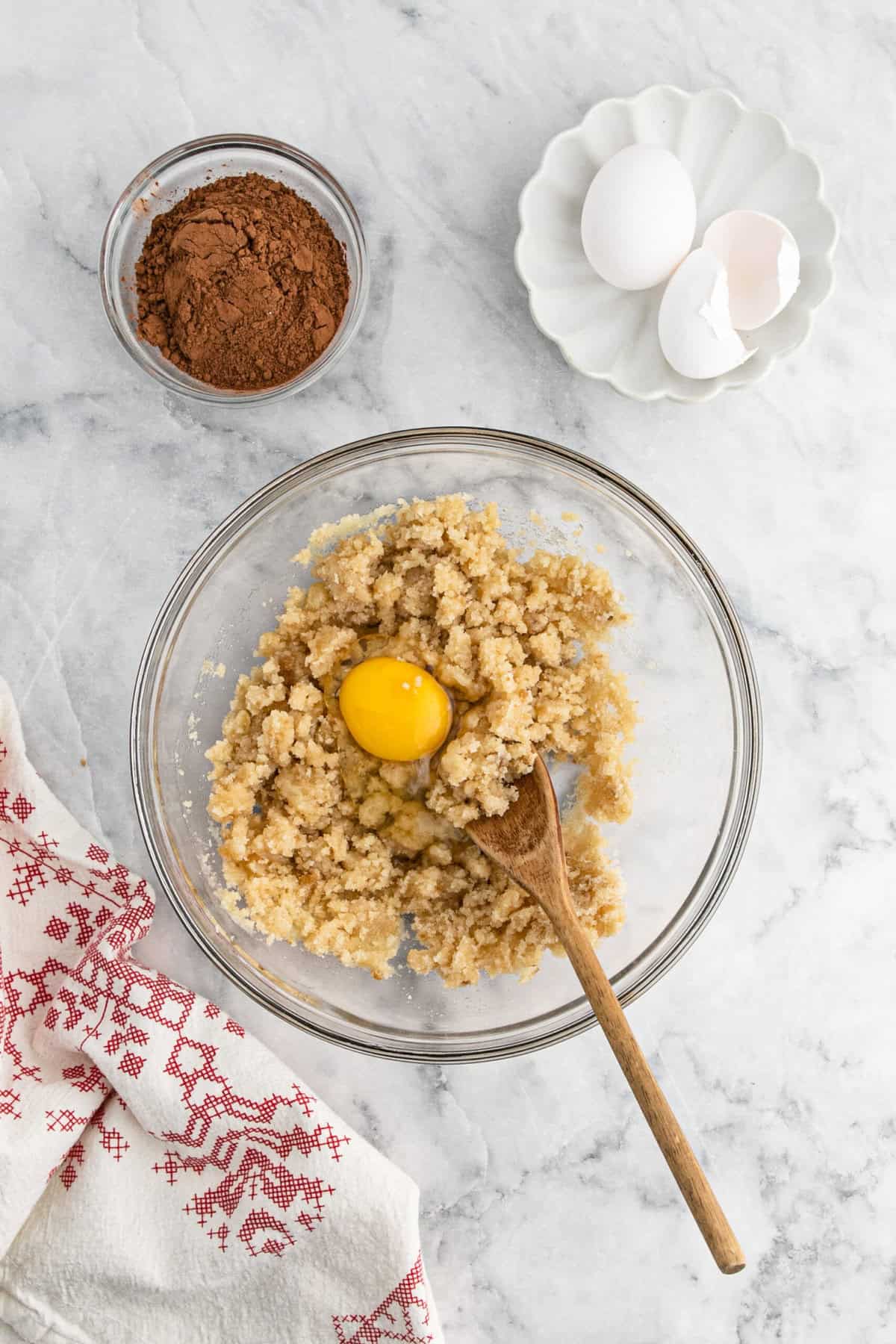 Eggs going into whisked together butter and sugars in glass bowl on marble countertop