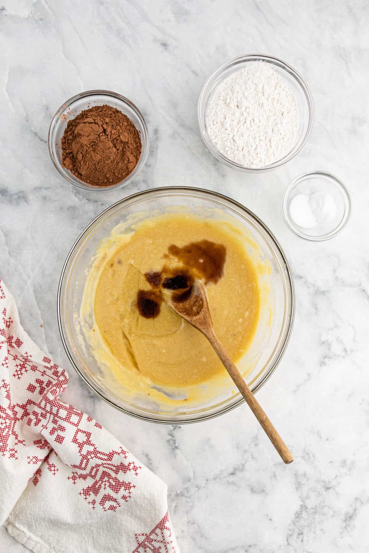 Vanilla and oil added to a brownie batter in a glass bowl on marble countertop