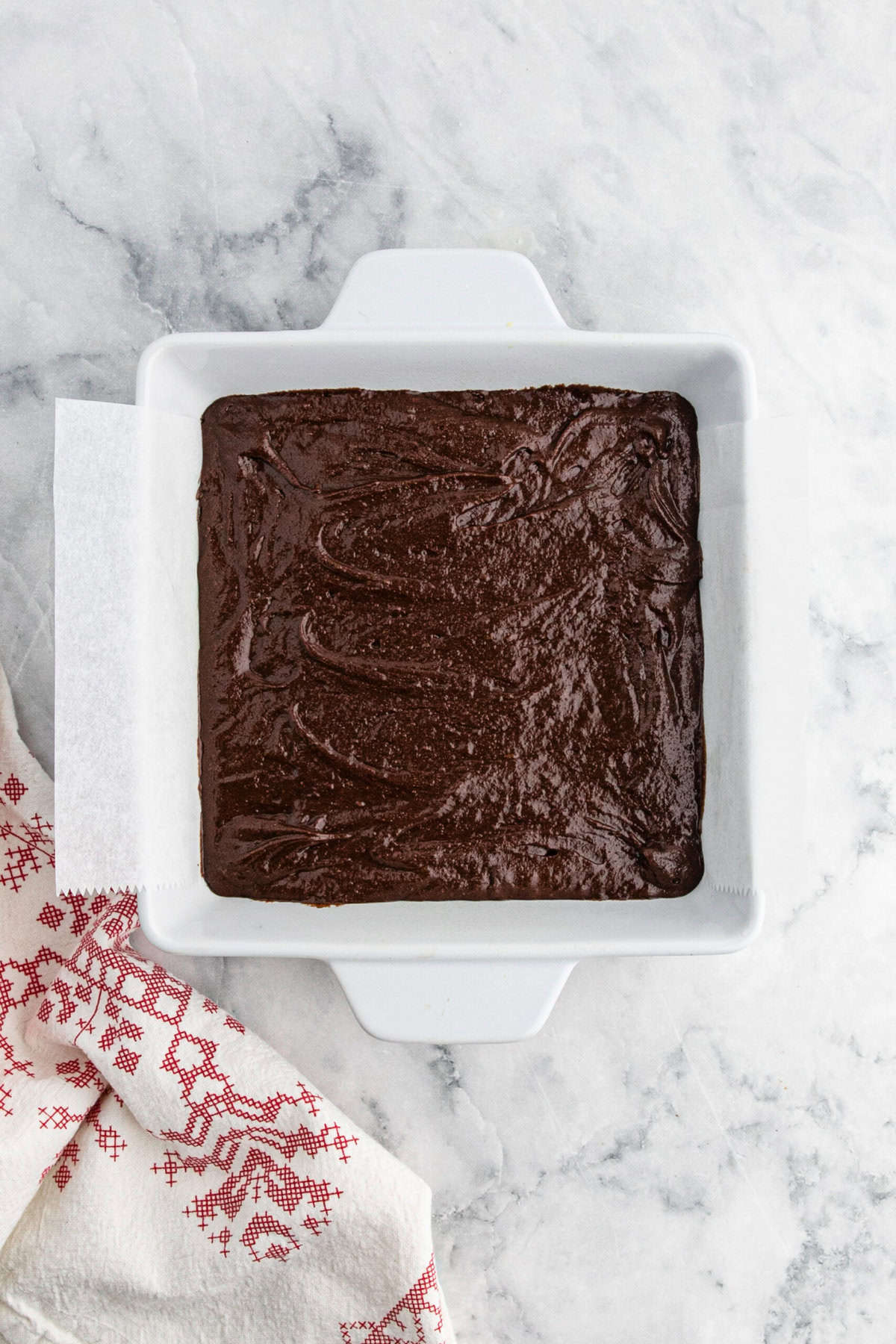 Chewy fudge brownie batter poured into a prepared pan on white countertop