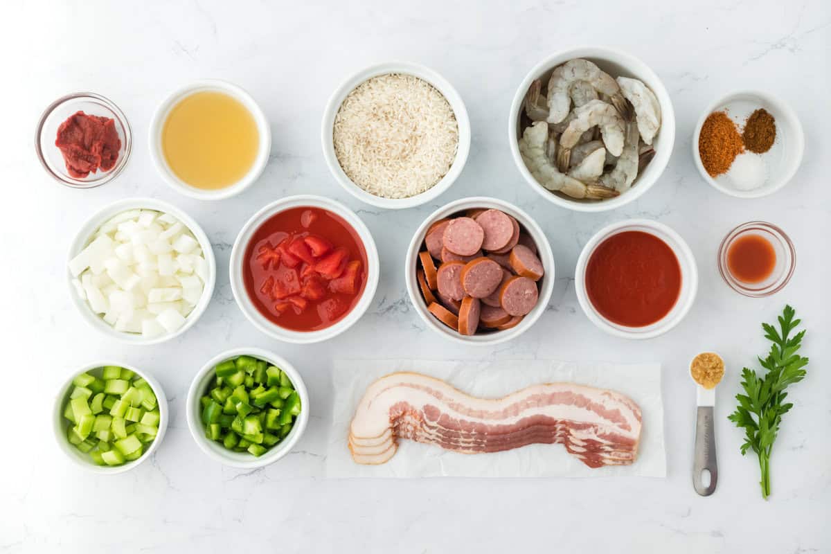 bacon, sausage, tomatoes, shrimp, spices and parsley in white bowls on a white background