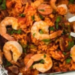 A close up overhead of a red rice recipe with shrimp on top on a white background being dug into with forks