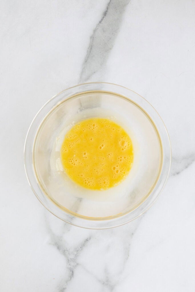 Heavy cream added to egg yolks in a glass bowl