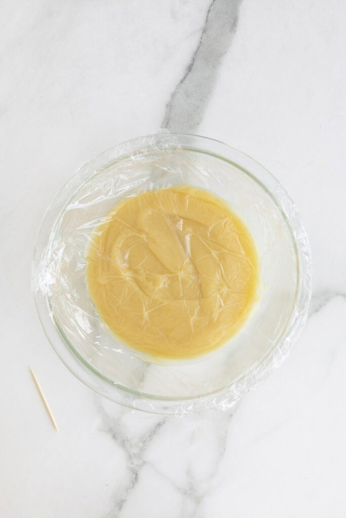 Plastic wrap covered vanilla pudding in a glass bowl