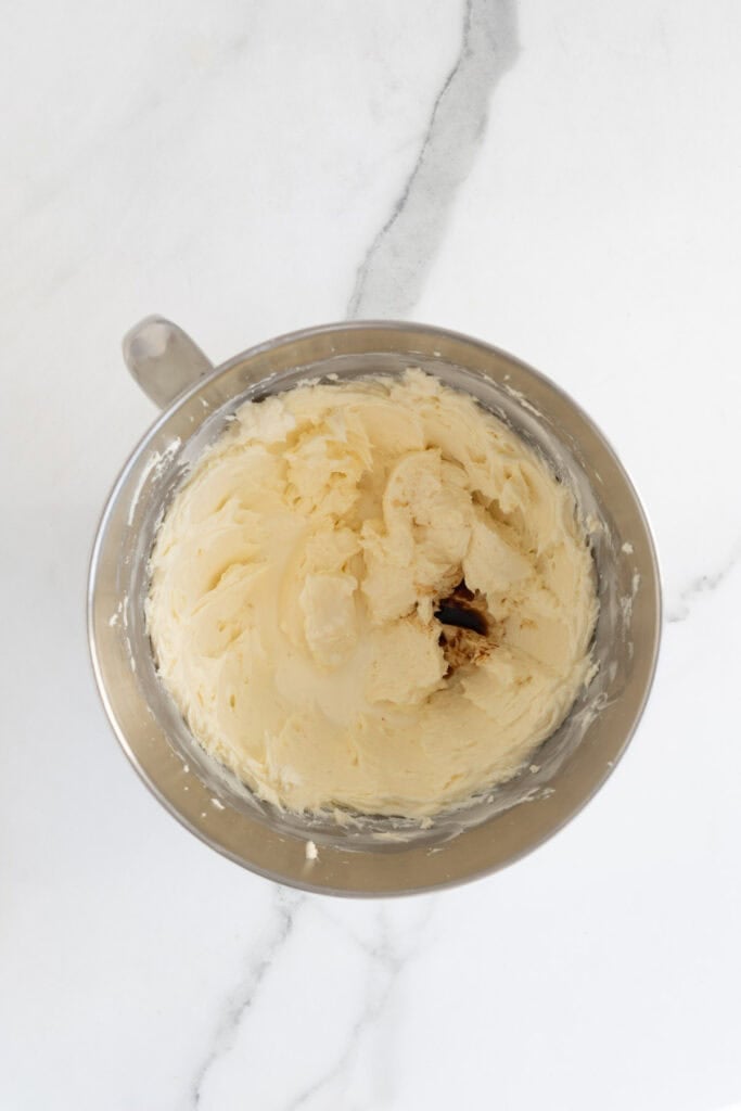 Vanilla extract and heavy cream added to cheesecake filling in a stand mixer bowl