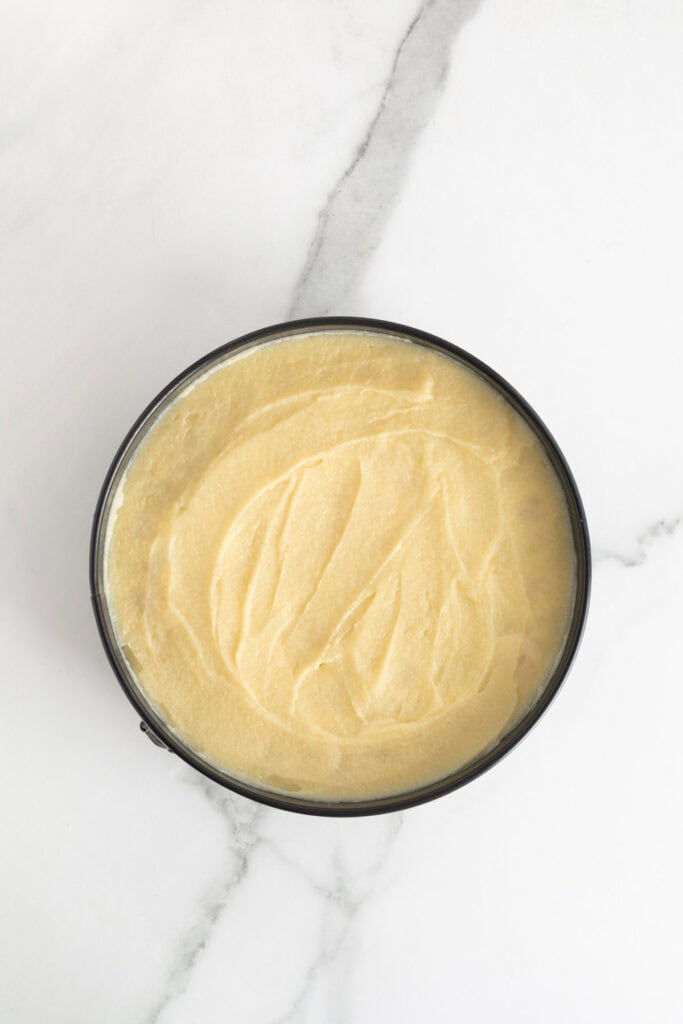 Banana pudding poured on top of sliced bananas in a springform pan