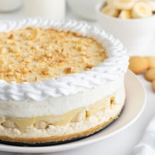 Banana pudding cheesecake on a white plate with nilla wafers and banana slices in the background