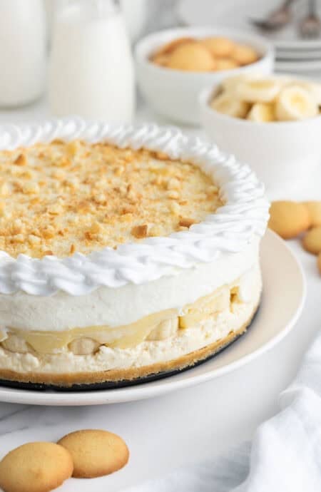 Banana pudding cheesecake on a white plate with nilla wafers and banana slices in the background