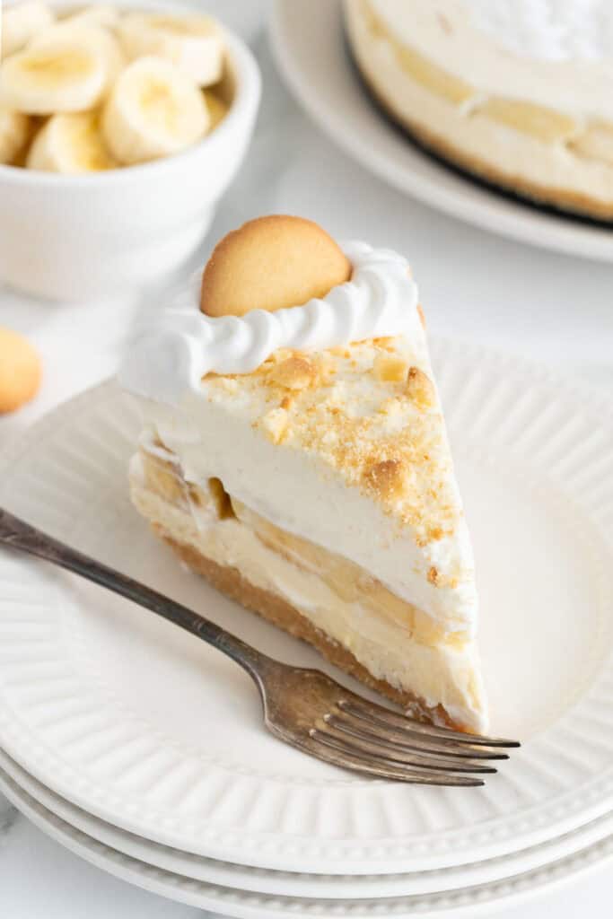 A slice of banana pudding cheesecake recipe on a white plate with a fork