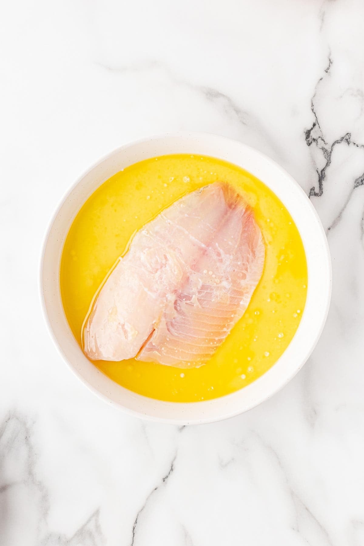 Raw fish fillet sitting in a bowl of melted butter