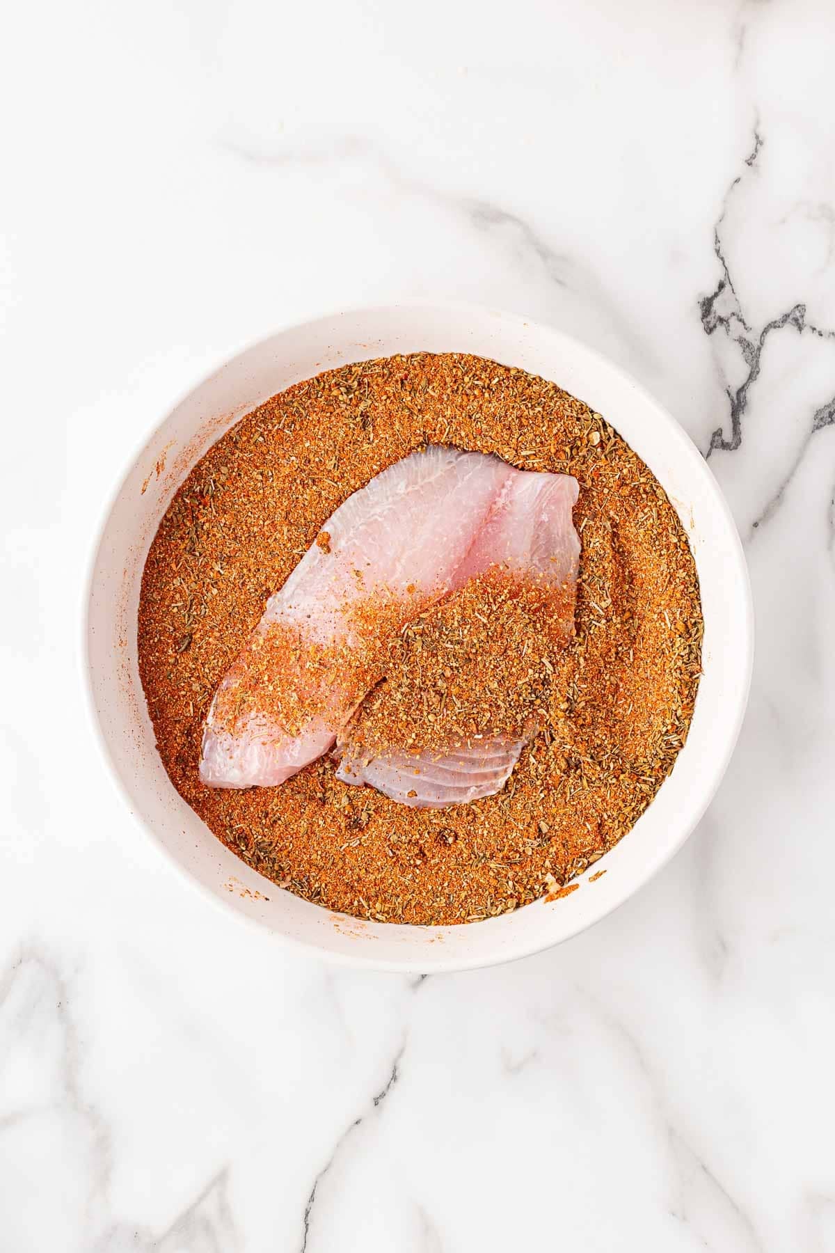Fish fillet coated in blackened seasoning in a shallow bowl