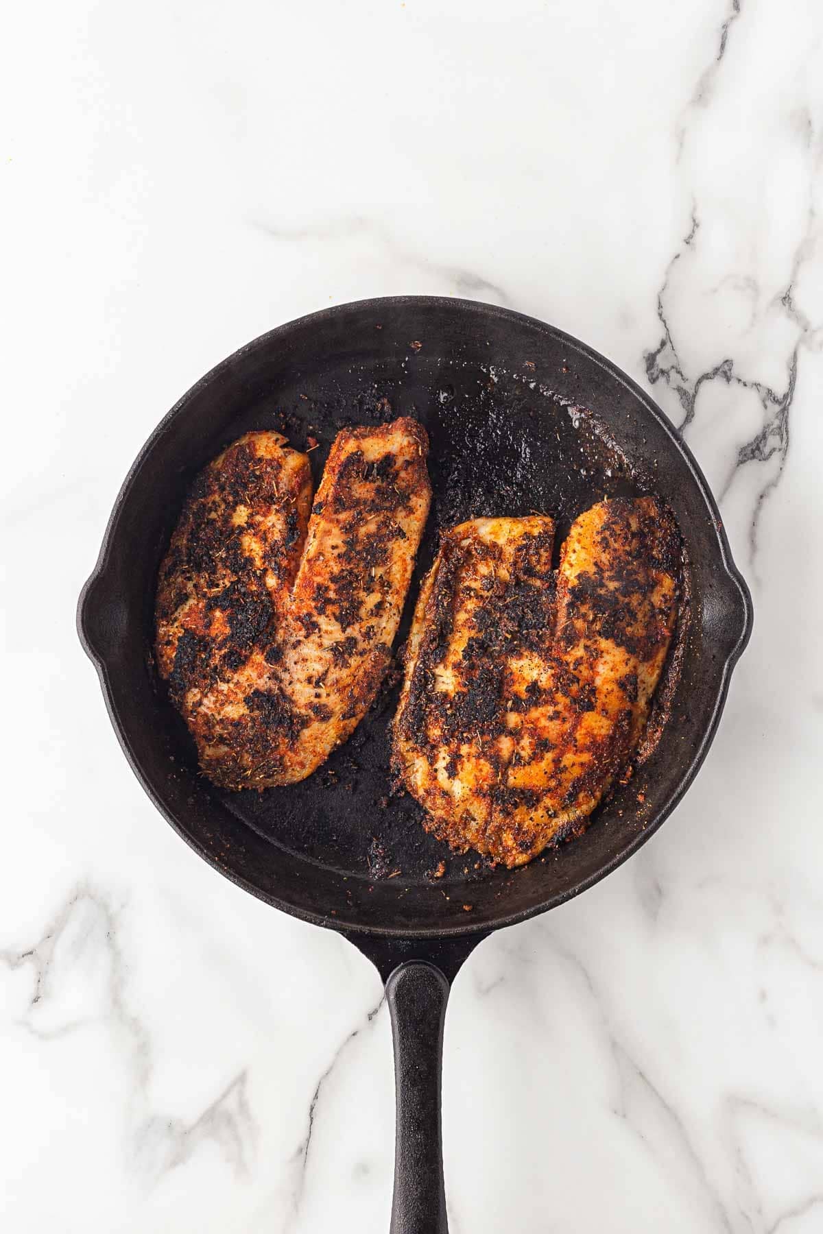 Blackened fish fillets cooking in a cast iron skillet