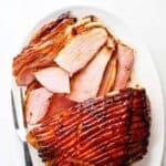 Honey baked ham on a platter with one end sliced up and the other whole with honey glaze.