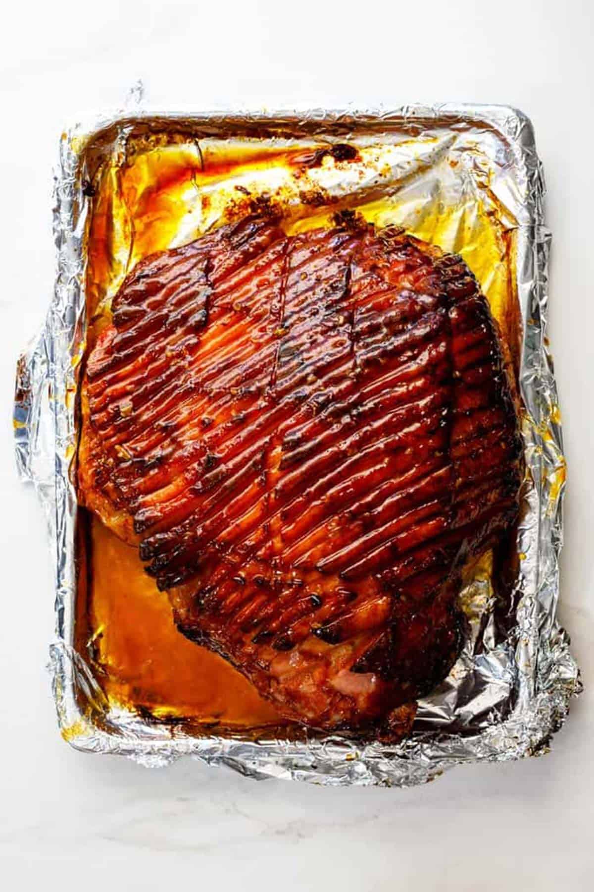 A whole honey baked ham fresh out of the oven with glaze spread everywhere