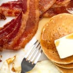 A close up of candied bacon strips with pancakes stacked with butter melted over it