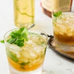 Two mint juleps with bourbon in the background and mint simple syrup