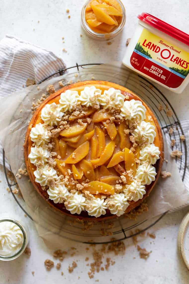 An overhead photo of a peach cheesecake with butter and peaches in background for the holidays