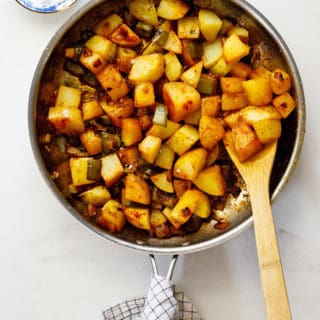 A large skillet of Smothered potatoes with a large spoon ready to serve