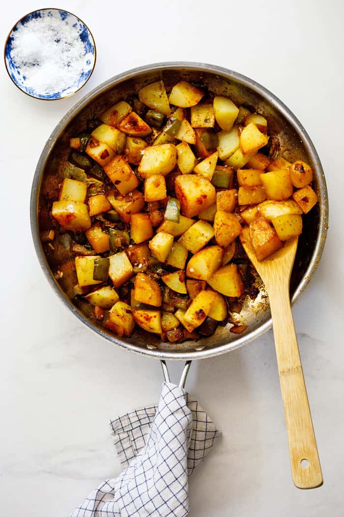 A large skillet of Smothered potatoes with a large spoon ready to serve