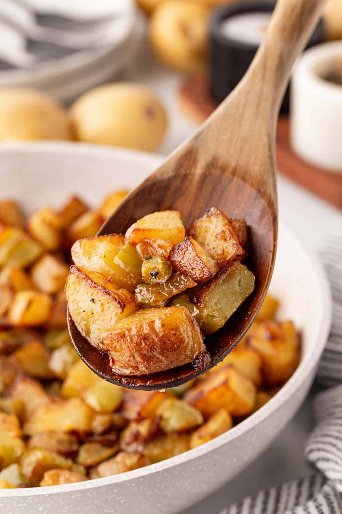 Wooden spoon holding crispy home fries above a skillet