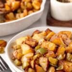 Bowl of crispy home fries with onions and green peppers served alongside the skillet