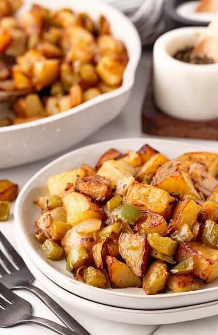 Bowl of crispy home fries with onions and green peppers served alongside the skillet