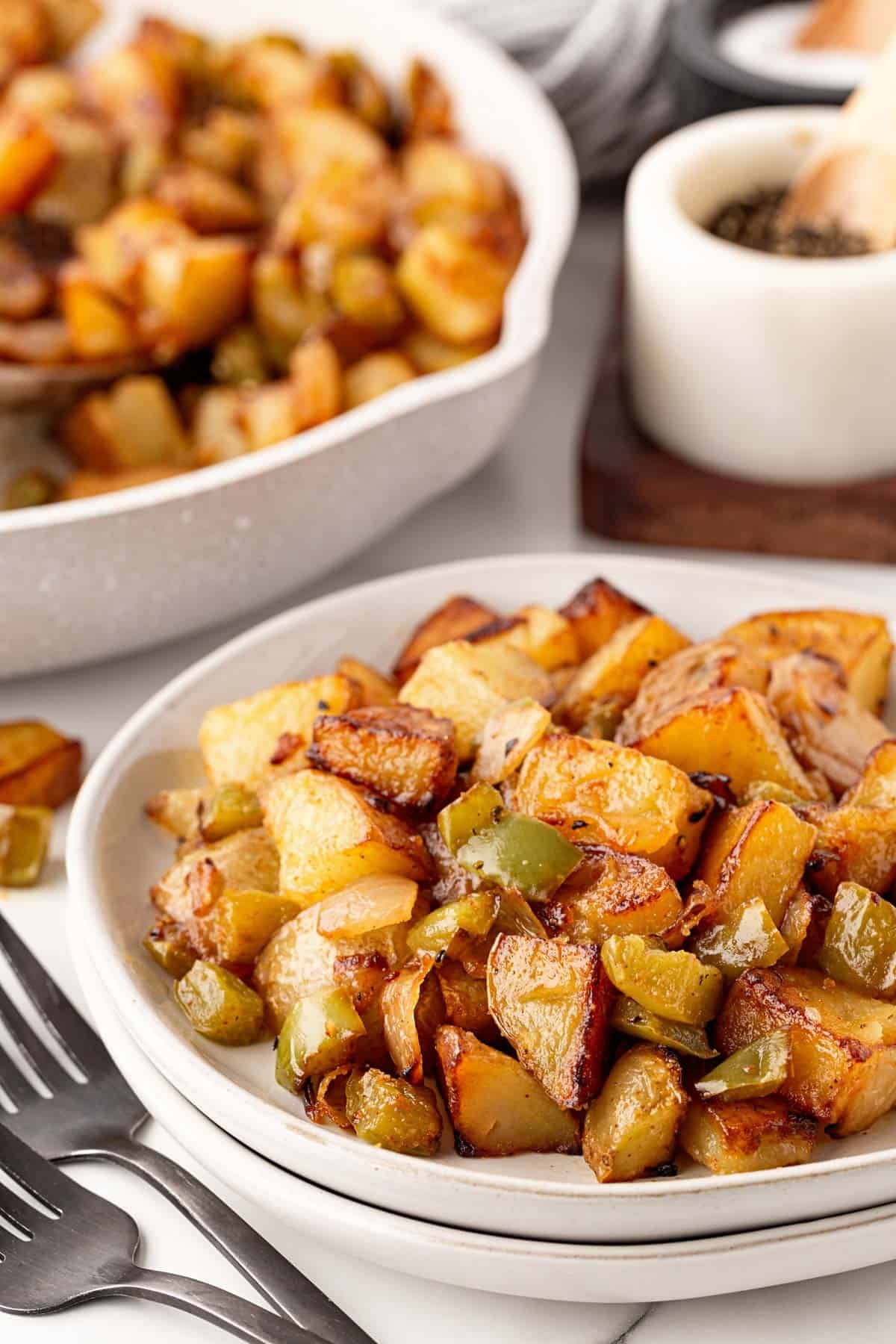 Bowl of crispy home fries with onions and green peppers served alongside the skillet