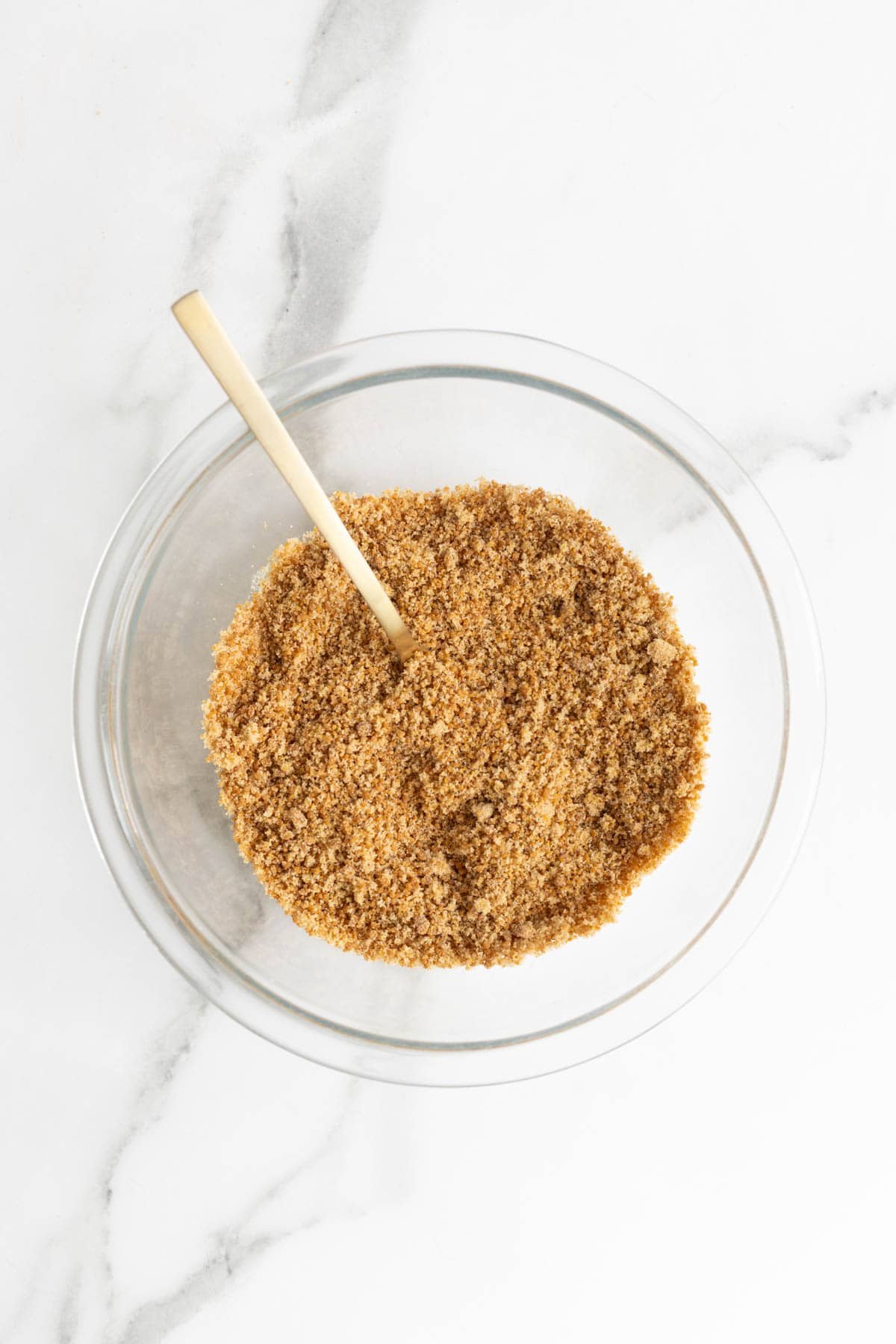 Brown sugar being stirred in a bowl with a gold spoon
