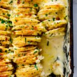 A giant pan of cheesy scalloped potatoes with a spoon lifting out a serving.