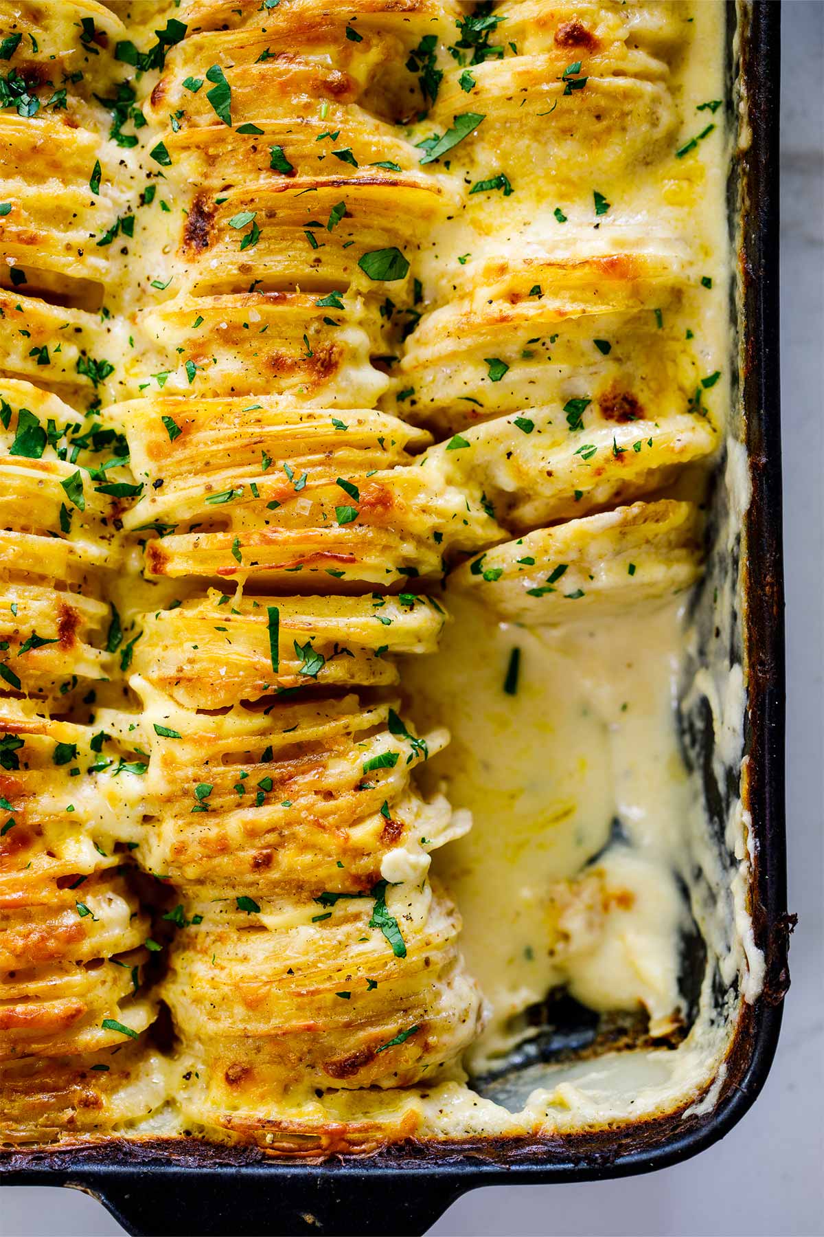 A giant pan of cheesy scalloped potatoes with a spoon lifting out a serving.